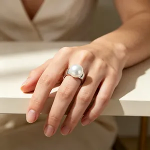 Nahaufnahme eines eleganten breiten Edelstahlrings mit einer großen Perle an einem Finger