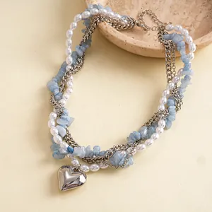 Detailopname van vintage gelaagde ketting met parels, blauwe stenen en hartvormige hanger
