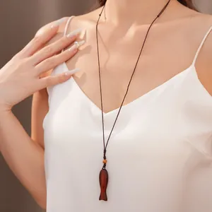 Eleganter Fischanhänger aus Holz an einer geflochtenen Kordel, von einem Model getragen