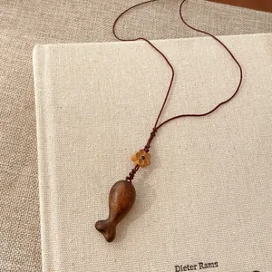 Detail eines handgeschnitzten Holzfisch-Anhängers mit kleiner Blumenperle an brauner Kordel.