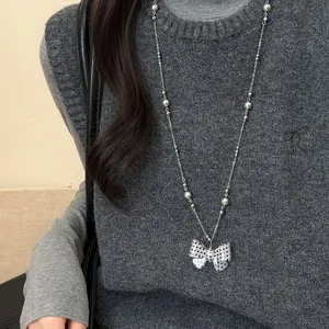 Polka dot strik parel trui ketting gedragen op een grijs vest voor een modieuze look