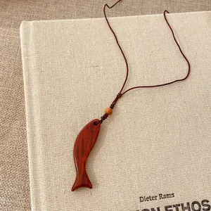 Detailaufnahme eines glatten Holz-Fisch-Anhängers an einer braunen geflochtenen Kette