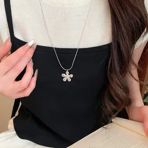 Close-up detail of a minimalist silver flower pendant necklace worn by a fashion model
