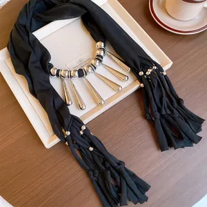 Gros plan du collier écharpe en tissu noir avec glands et perles en métal argenté.