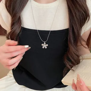 Close-up view of a minimalist silver flower pendant necklace worn by an elegant model