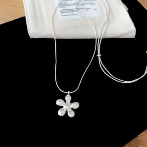 Detailed close-up of a minimalist silver flower pendant necklace resting on black velvet