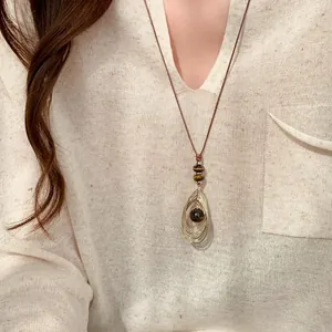 Dichtbij van een vintage tijgeroog hanger ketting gedragen op een crème v-hals trui