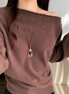 Detailopname van een retro ketting met tijgeroog hanger op een bruine trui achtergrond