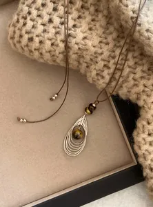 Detailweergave van een retro hanger met tijgeroogsteen en een bruin leren koord.