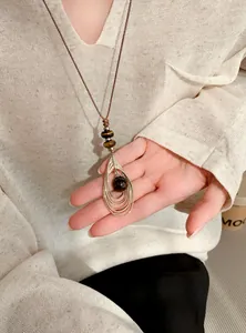 Detailopname van vintage lederen koordketting met druppelhanger en tijgeroogsteen.