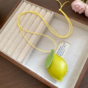 Detailaufnahme einer Lederkette mit zitronenförmigem Anhänger, grünem Blatt und weißen Nähten.