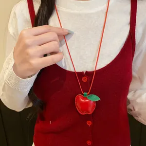 Nahaufnahme einer süßen roten Apfel-Anhänger-Halskette aus Leder auf Strickweste.