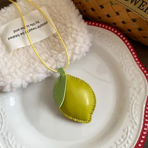 Detailaufnahme des zitronenförmigen Lederanhängers an einer gelben Kordelkette.