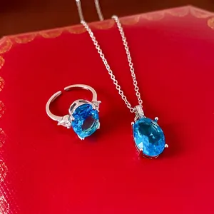 Elegantes Schmuckset mit ovalem blauem Zirkon, Halskette und Ring auf rotem Grund