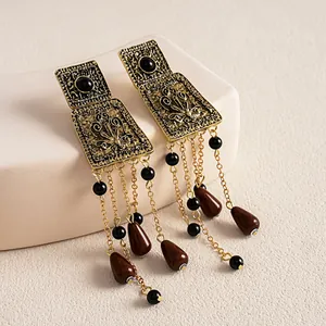 Close-up detail of vintage distressed gold metal earrings with brown teardrop tassel charms