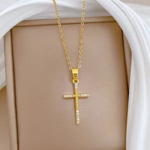Gros plan d'un collier croix en acier titane doré avec pierres blanches étincelantes.