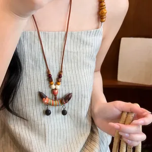 Detail van een etnische houten kralenketting met erwtenhanger op een gestreepte top.