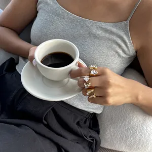 Lifestyle-Ansicht goldener Edelstahlringe mit Zirkonia, Modell hält eine Kaffeetasse.