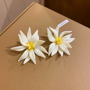 Nahaufnahme von eleganten weißen Harzblumen-Ohrringen mit gelben Kristallmitten auf Karton.