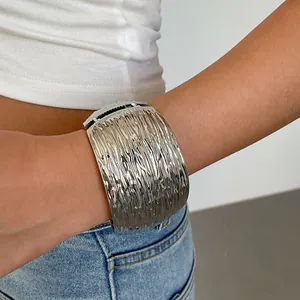 Gedetailleerde close-up van brede zilveren metalen manchetarmband met geplooide textuur op arm