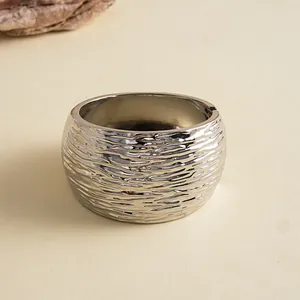Close-up van een zilveren metalen manchetarmband met een kenmerkende gerimpelde golftextuur.