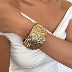 Detailopname van een gouden brede manchetarmband met een gehamerde textuur