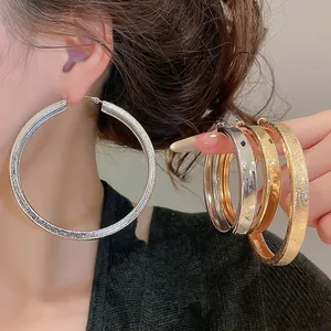 Close-up of oversized silver and gold hoop earrings with glitter and smooth finishes.
