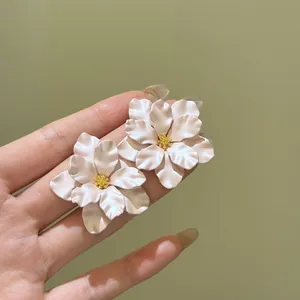 Detaillierte Makroansicht von eleganten weißen Kamelien-Ohrsteckern in einer Hand