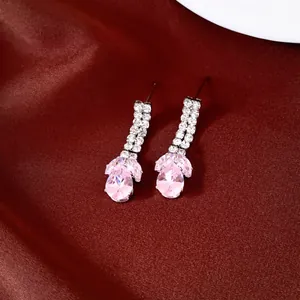 Gros plan d'élégantes boucles d'oreilles goutte en zircone rose avec strass sur soie rouge.