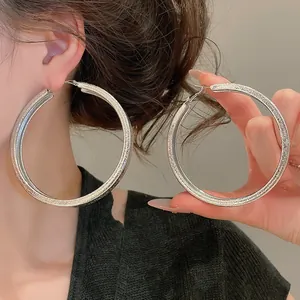 Close-up of large silver textured hoop earrings showcasing glittery wrinkled surface finish.