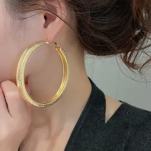 Close-up shot showing the unique textured surface of large gold hoop earrings on ear.