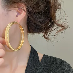 Close-up of a large gold hoop earring with textured finish worn by an Asian model.
