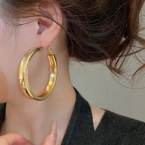 Detail shot of oversized glossy gold hoop earrings on a model for a bold fashion look