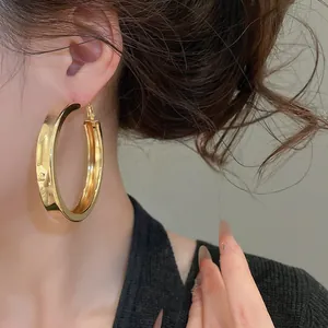 Detailed side view of a large polished gold hoop earring worn by an Asian model