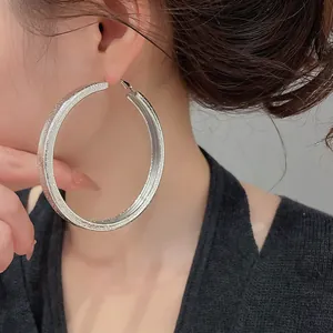 Detailed macro view of large silver textured hoop earrings worn by an elegant model