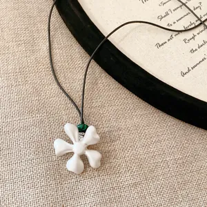 Dettaglio di una collana con pendente a fiore in ceramica bianca e una perla verde su cordino