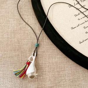 Dettaglio di una collana con nappina multicolore e ciondolo argento su cordoncino.