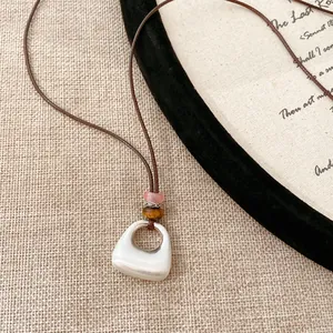 Dettaglio collana in corda di cuoio con perle occhio di tigre e pendente geometrico