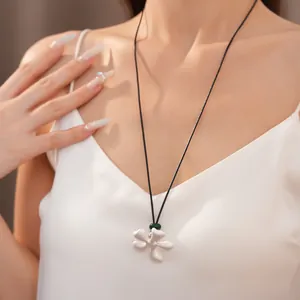 Dettaglio ravvicinato di una collana con ciondolo a fiore in ceramica bianca e perla verde