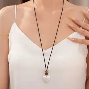 Primo piano di una collana con ciondolo a cuore e perle in ceramica su una modella