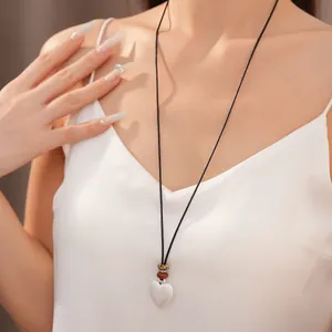 Dettaglio di una collana con ciondolo a cuore bianco e perline di ceramica su corda