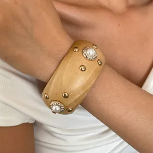 Detailopname van retro houten armband met gouden klinknagels en parels om de pols