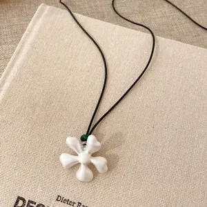 Vista dettagliata di una collana con ciondolo a fiore bianco opaco e perle ceramiche su cordino