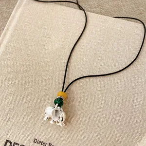 Dettaglio macro del ciondolo a forma di elefante con malachite e perline gialle su cordoncino.
