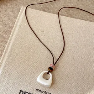 Dettaglio di una collana con ciondolo in ceramica su cordino di cuoio marrone sopra un libro