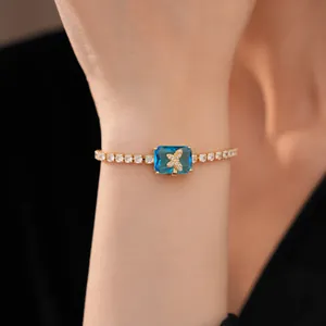 Primo piano di un bracciale a farfalla placcato oro con zircone blu quadrato al polso.