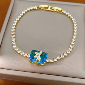 Dettaglio del bracciale tennis dorato con pietra blu quadrata e ciondolo a farfalla