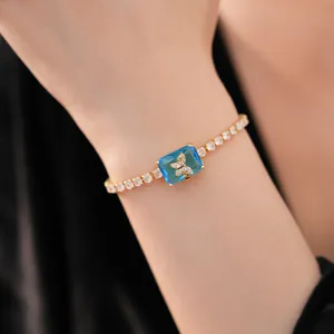 Vista dettagliata di un bracciale placcato oro con gemma blu quadrata e farfalla zirconi.
