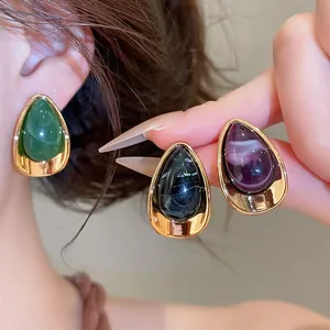 Gros plan de boucles d'oreilles en résine en forme de larme, coloris vert, noir et violet.