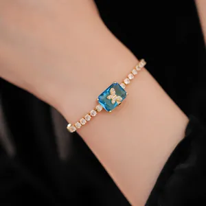 Dettaglio del bracciale con zircone blu e un motivo a farfalla dorata brillante sul polso.